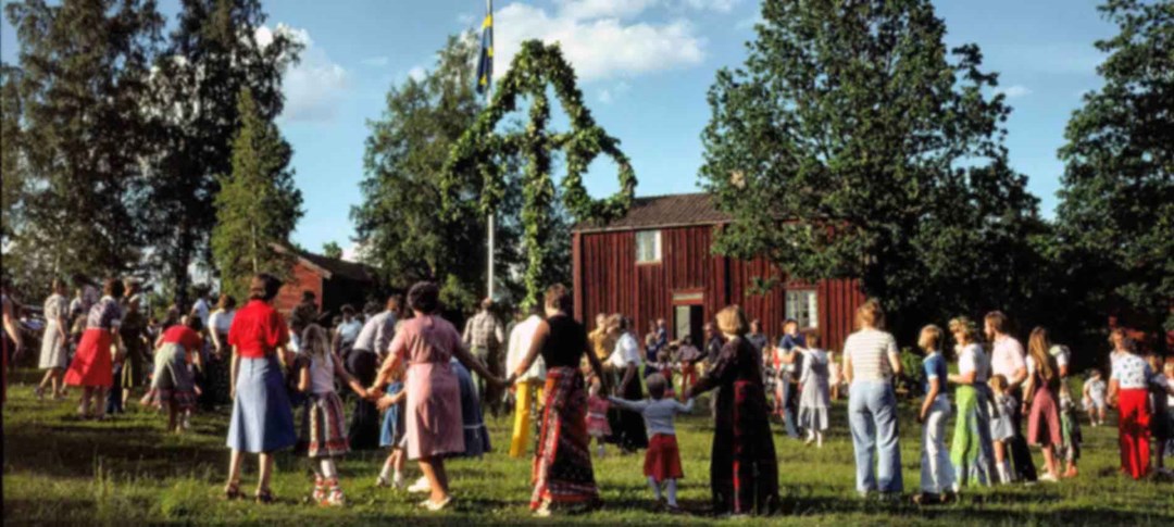 Människor dansar runt midsommarstång på midsommarafton